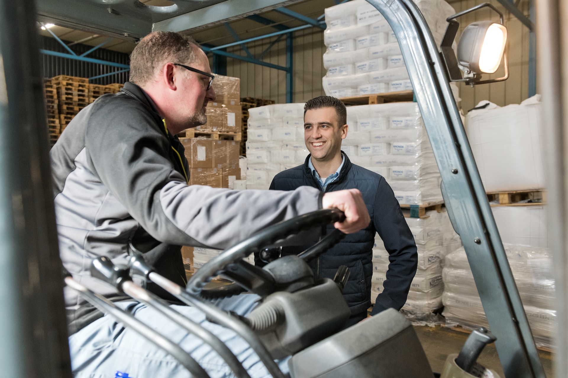 Twee collega’s overleggen bij heftruck in magazijn.