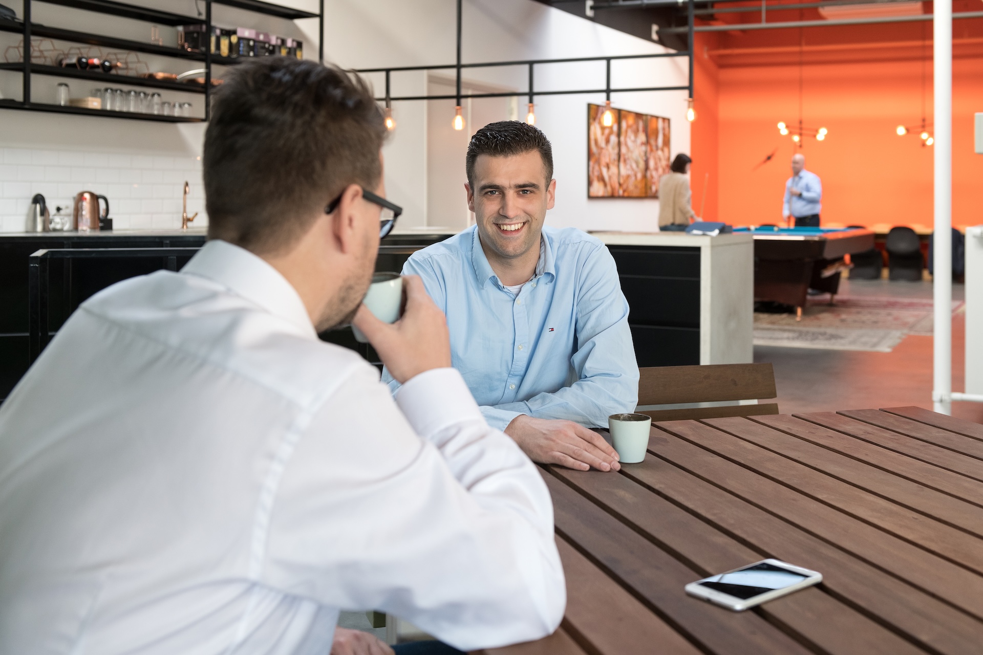 Twee collega’s drinken koffie en praten in kantoor.