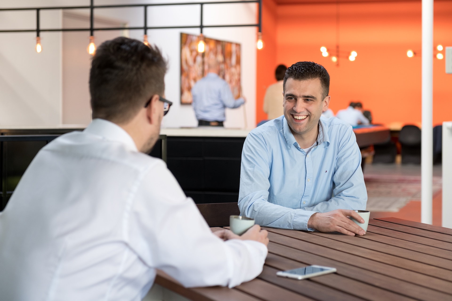 Twee collega’s in gesprek aan tafel in kantooromgeving.