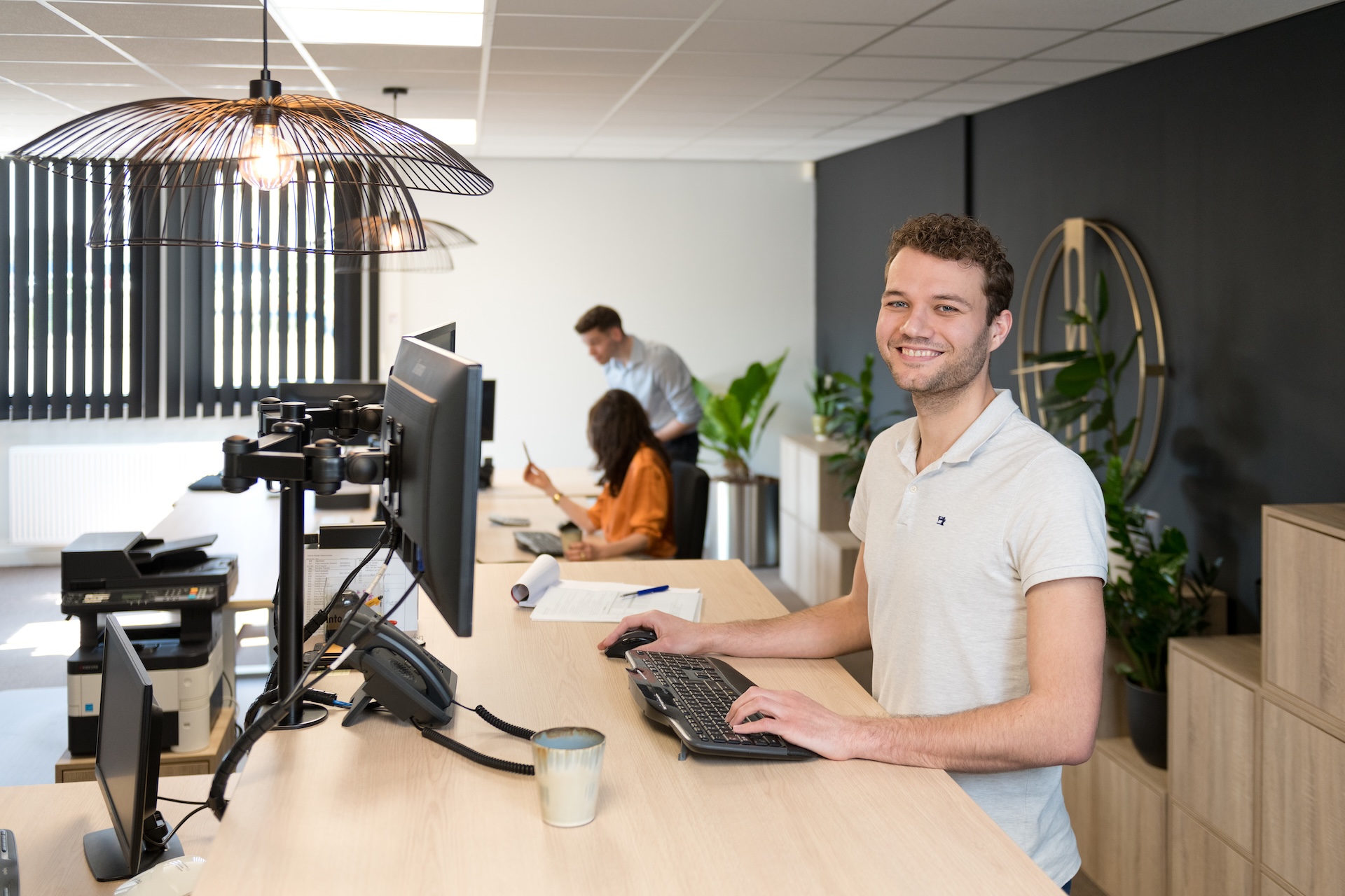 Kantoormedewerker werkt achter bureau, collega’s op achtergrond.