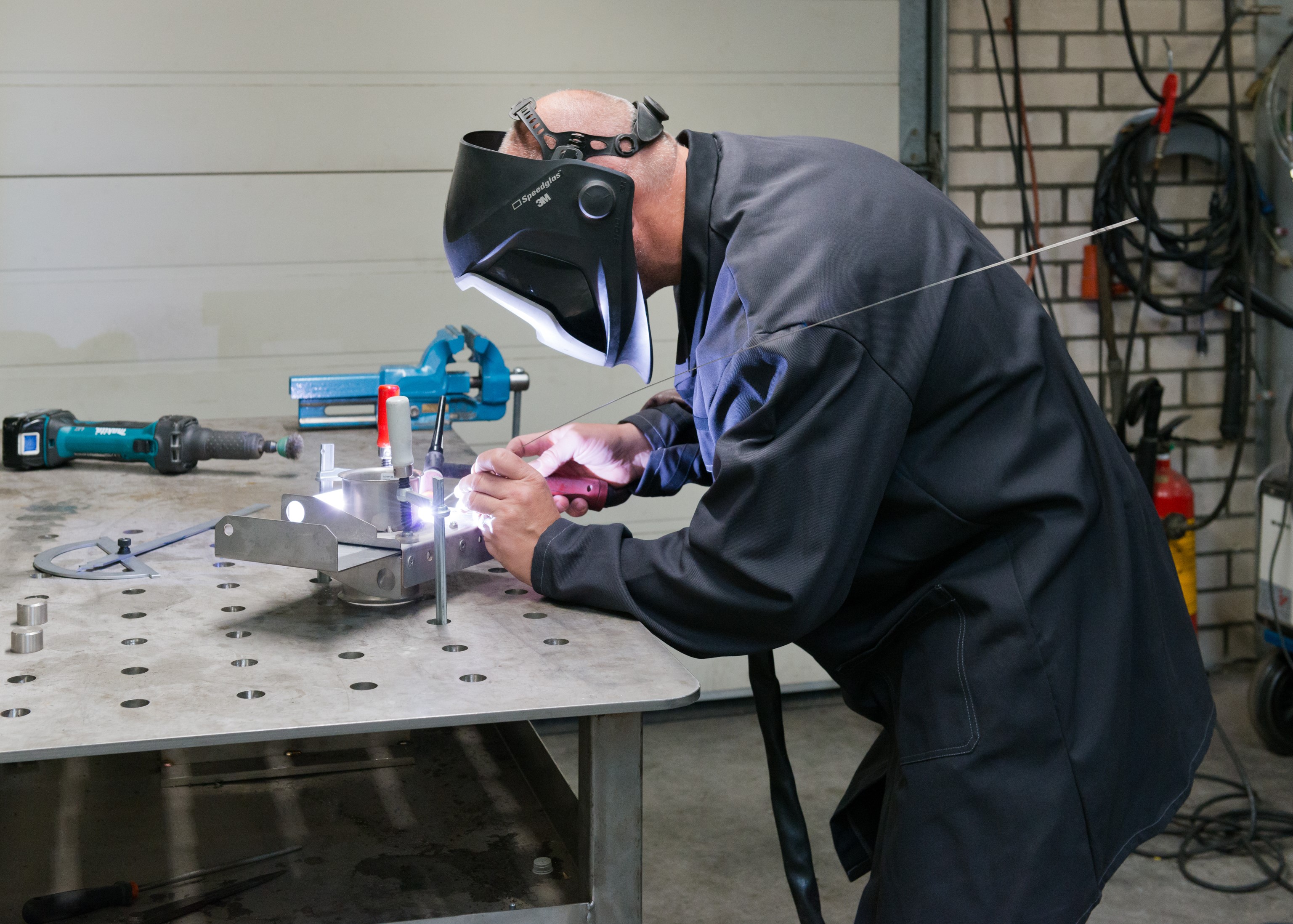 Lasser werkt met beschermhelm aan metalen onderdeel.