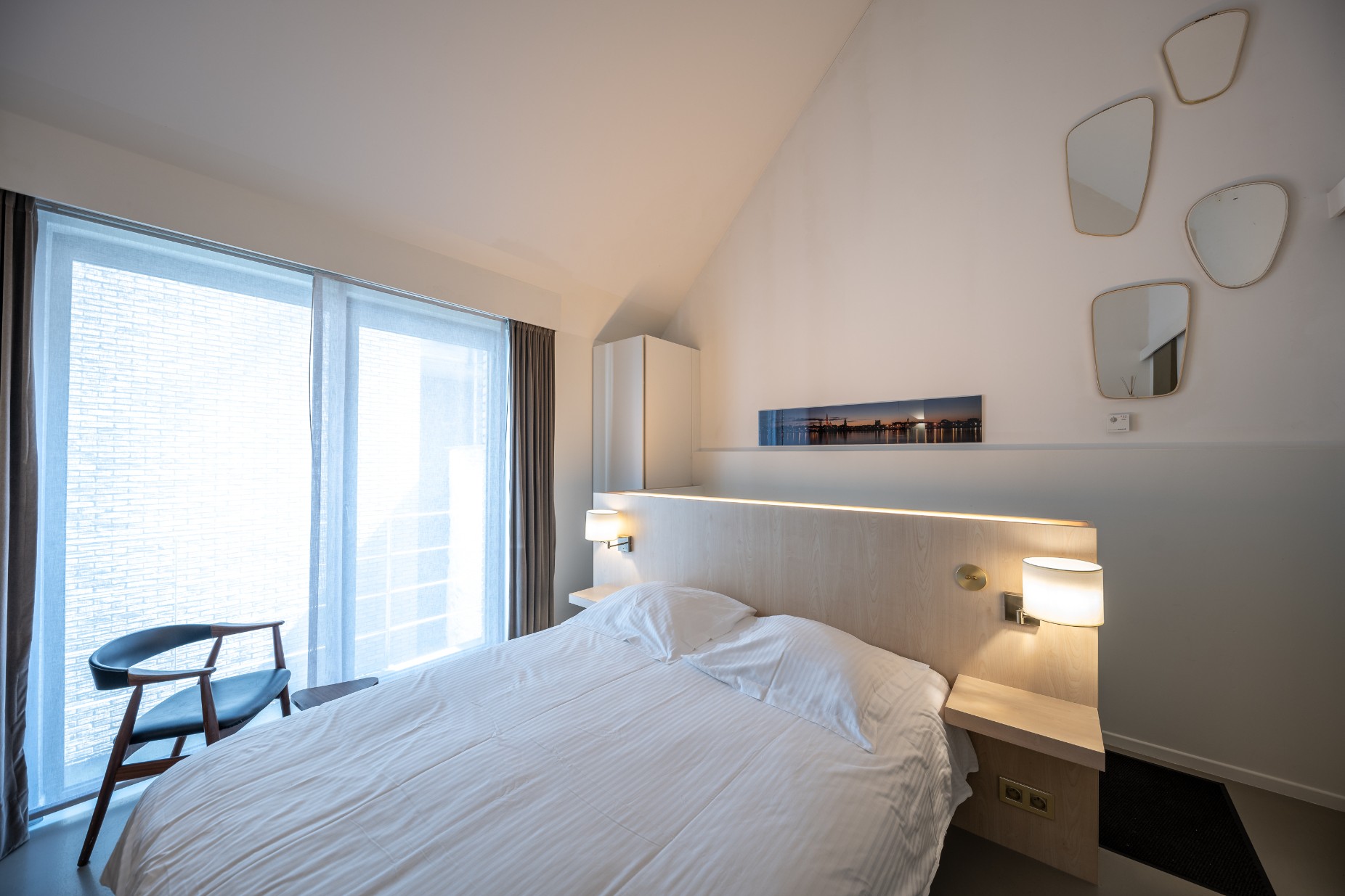 Queen bed by floor-to-ceiling windows in the De Koninck Room