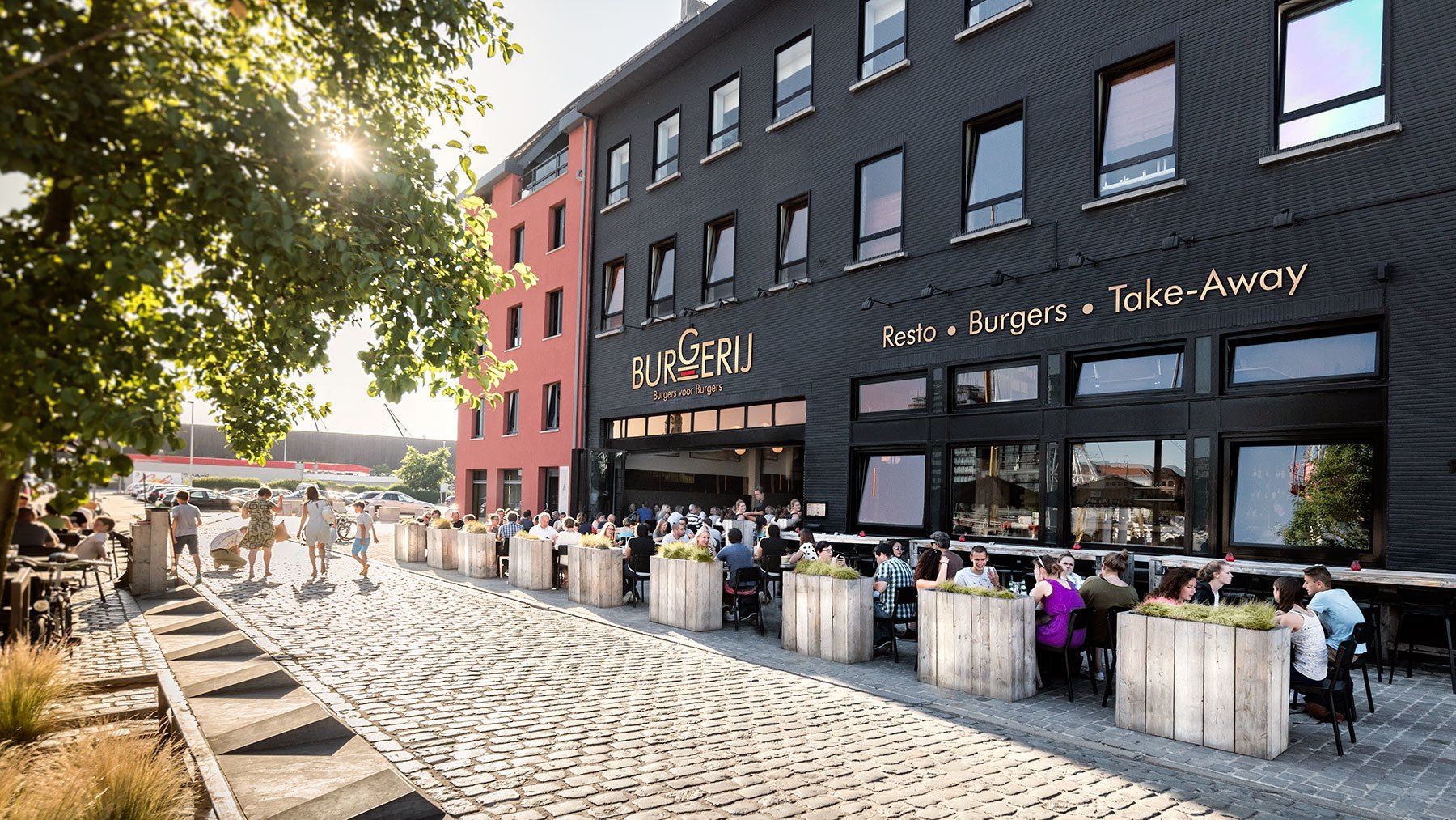 Burger restaurant with outdoor terrace seating in modern urban neighbourhood courtyard.