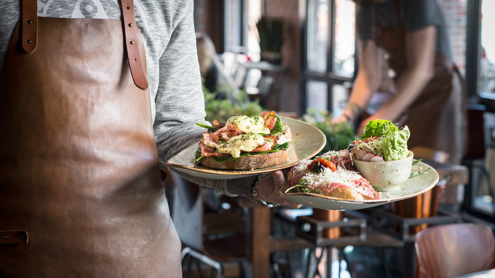Server presenting gourmet plated dishes in upscale dining area with brick facade.
