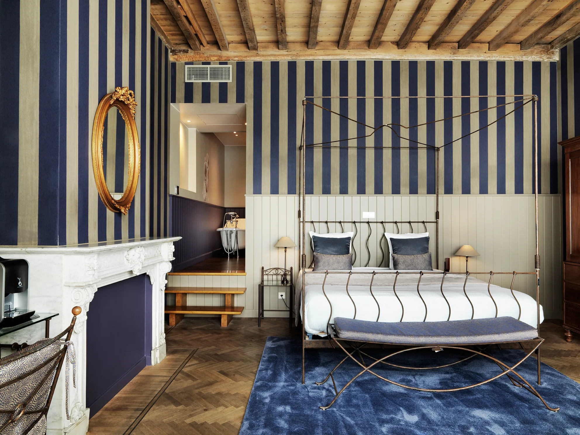 Luxe slaapkamer suite met hemelbed, gestreept behang en open haard.