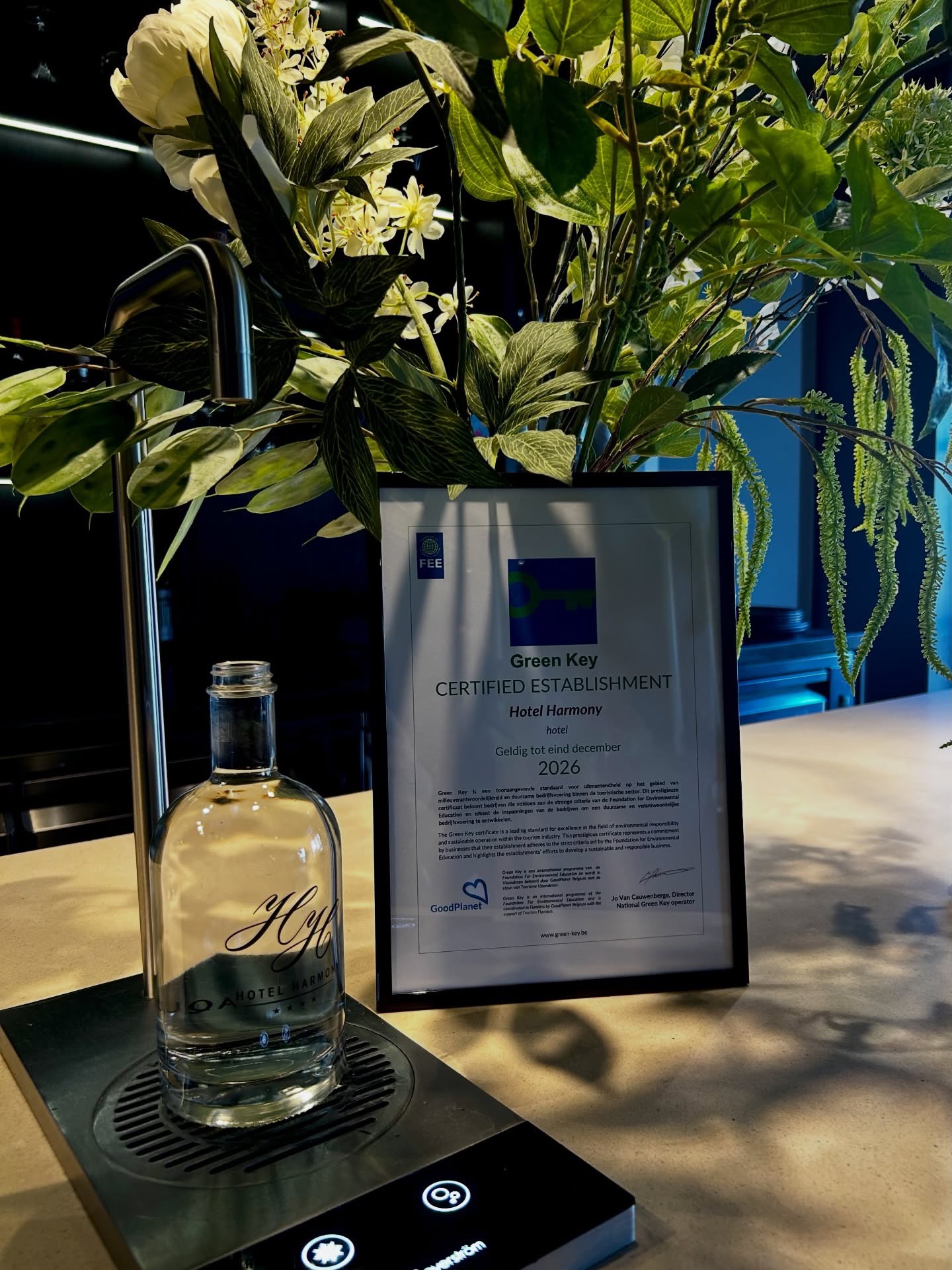 Hotel Harmony Green Key-certificering getoond met verse planten en fles water met hotelmerk.