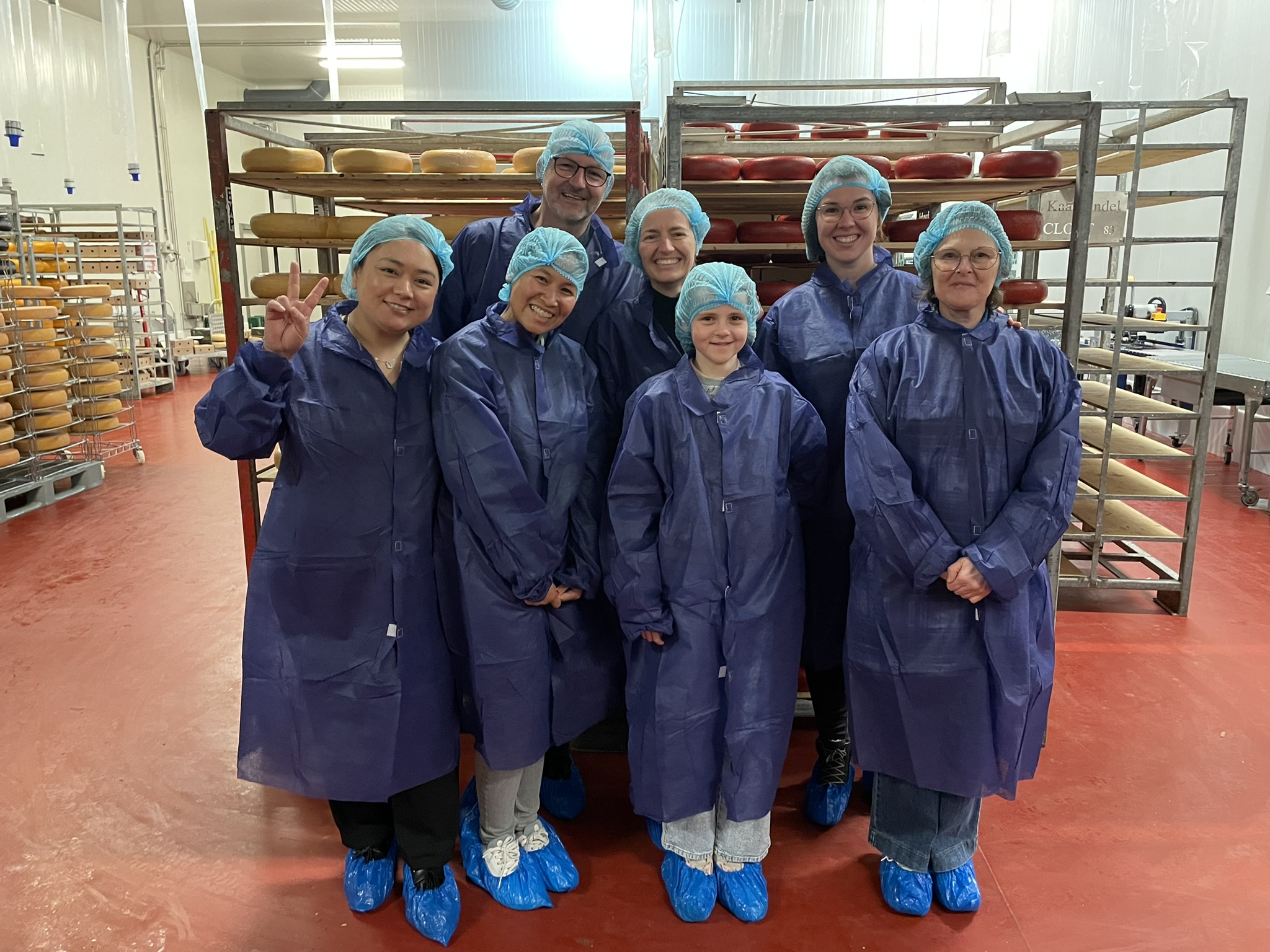 Groep medewerkers in beschermende kleding bij een kaasproductiefaciliteit met haarnetjes.