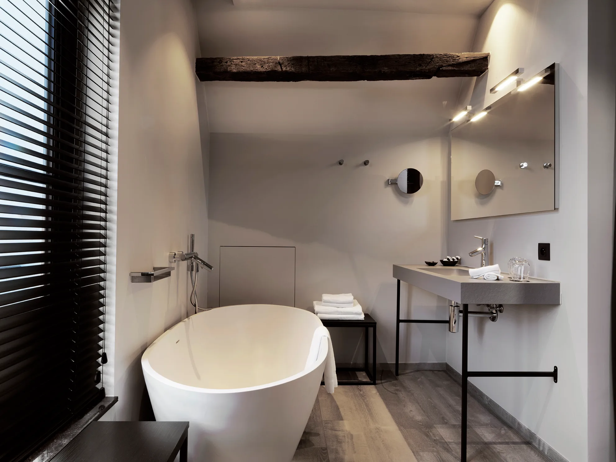 Moderne badkamer met vrijstaand wit bad, opbouw wastafel en rustieke houten plafondbalk.