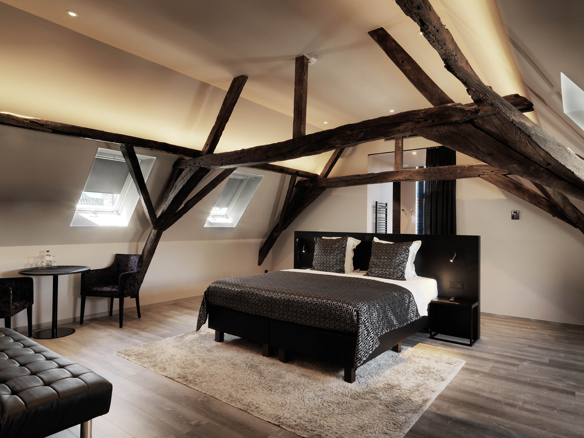 Luxe zolder slaapkamer suite met donkere houten balken en dakramen.