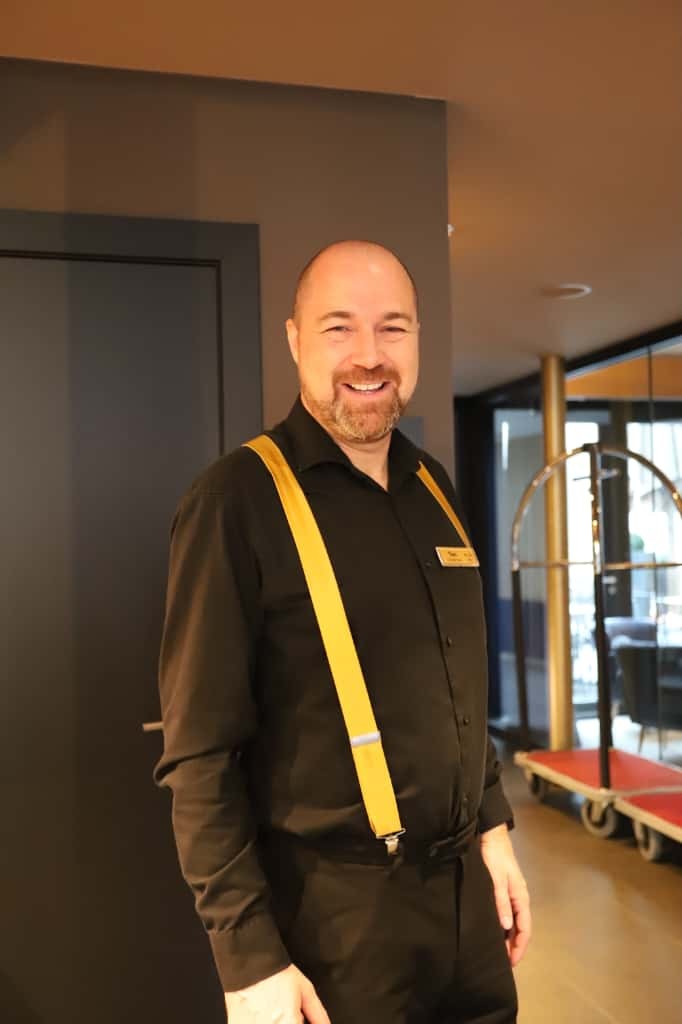 Medewerker in uniform glimlacht binnen in een modern ingerichte horecaruimte.