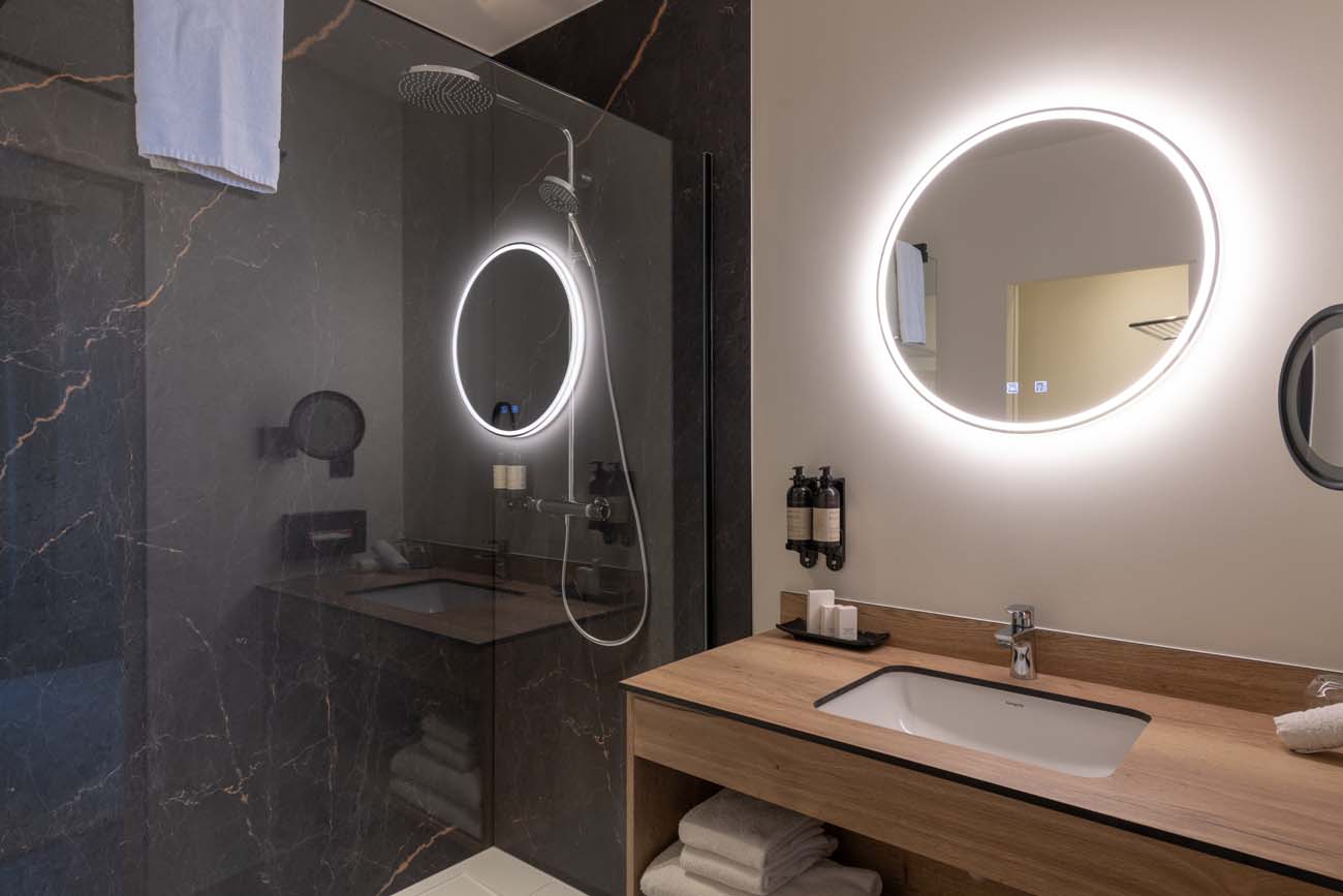 Badkamer met marmeren douche, verlichte spiegel en houten wastafelmeubel