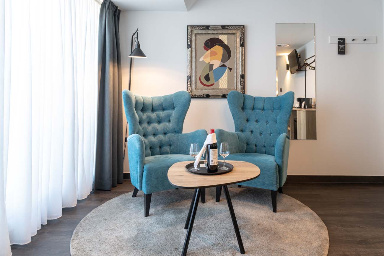 Zithoek met turquoise oorfauteuils en een glas wijn