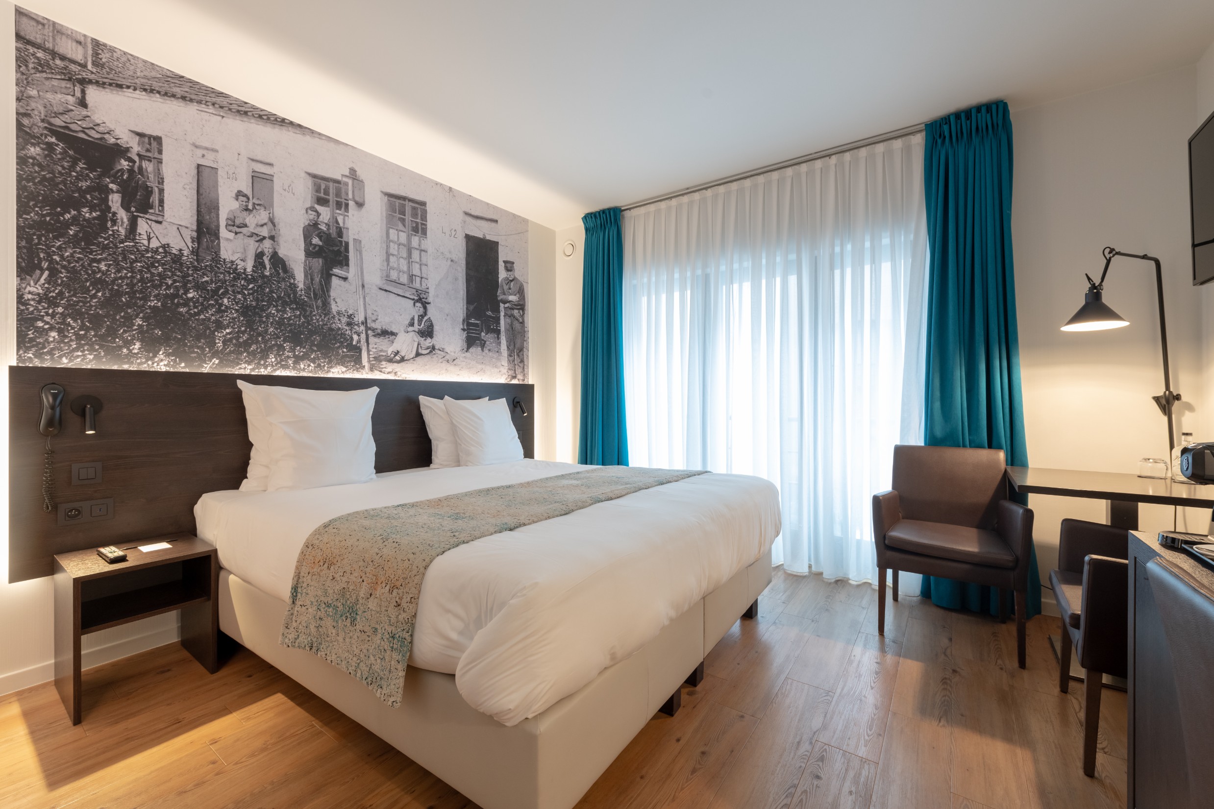 Hotelkamer met wit beddengoed, turquoise gordijnen en historisch wandkunstwerk