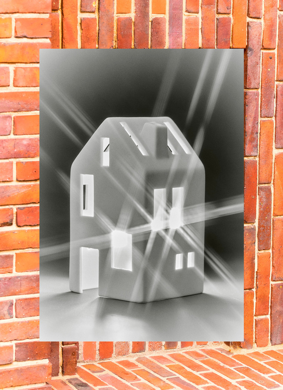 Ein stilisiertes Haus aus hellem Material steht vor einer roten Backsteinwand. Das Haus scheint durch Lichtstrahlen hervorgehoben zu werden, die von innen nach außen scheinen. Die Darstellung wirkt abstrakt und modern.