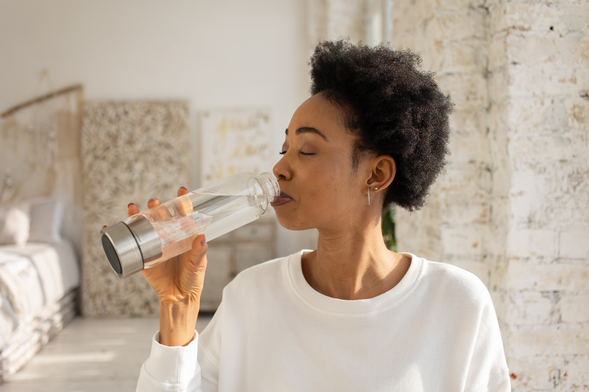 Woman standing indoors drinking water from a water bottle.