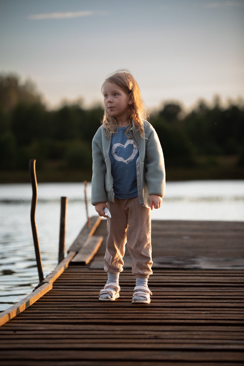 A little girl crouching on a dock near a lake · Free Stock Photo
