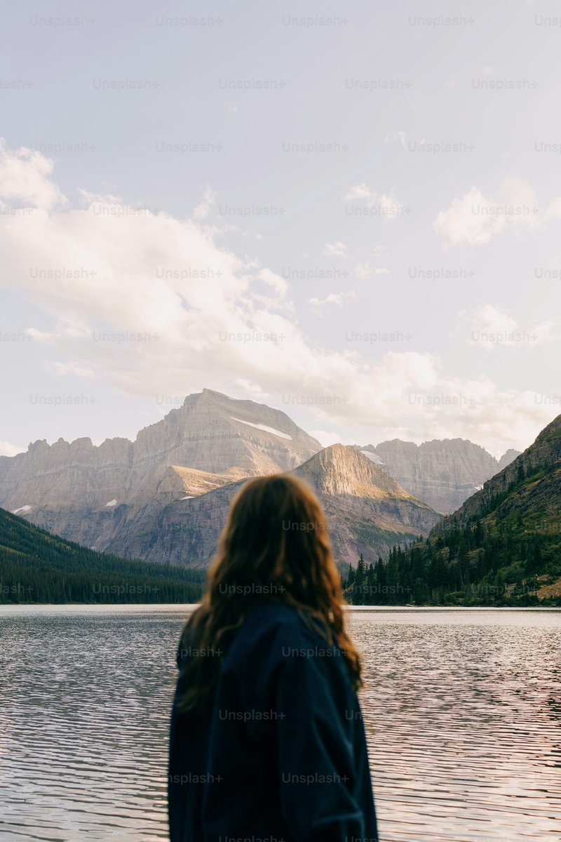A woman standing in front of a lake with mountains in the background photo – Forest Image on Unsplash