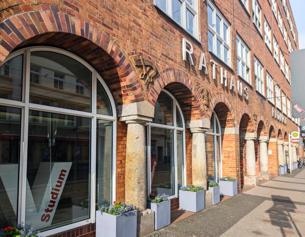 Fassade des Rathauses mit großen Fenstern und Pflanzkästen aus Stein im Vordergrund.