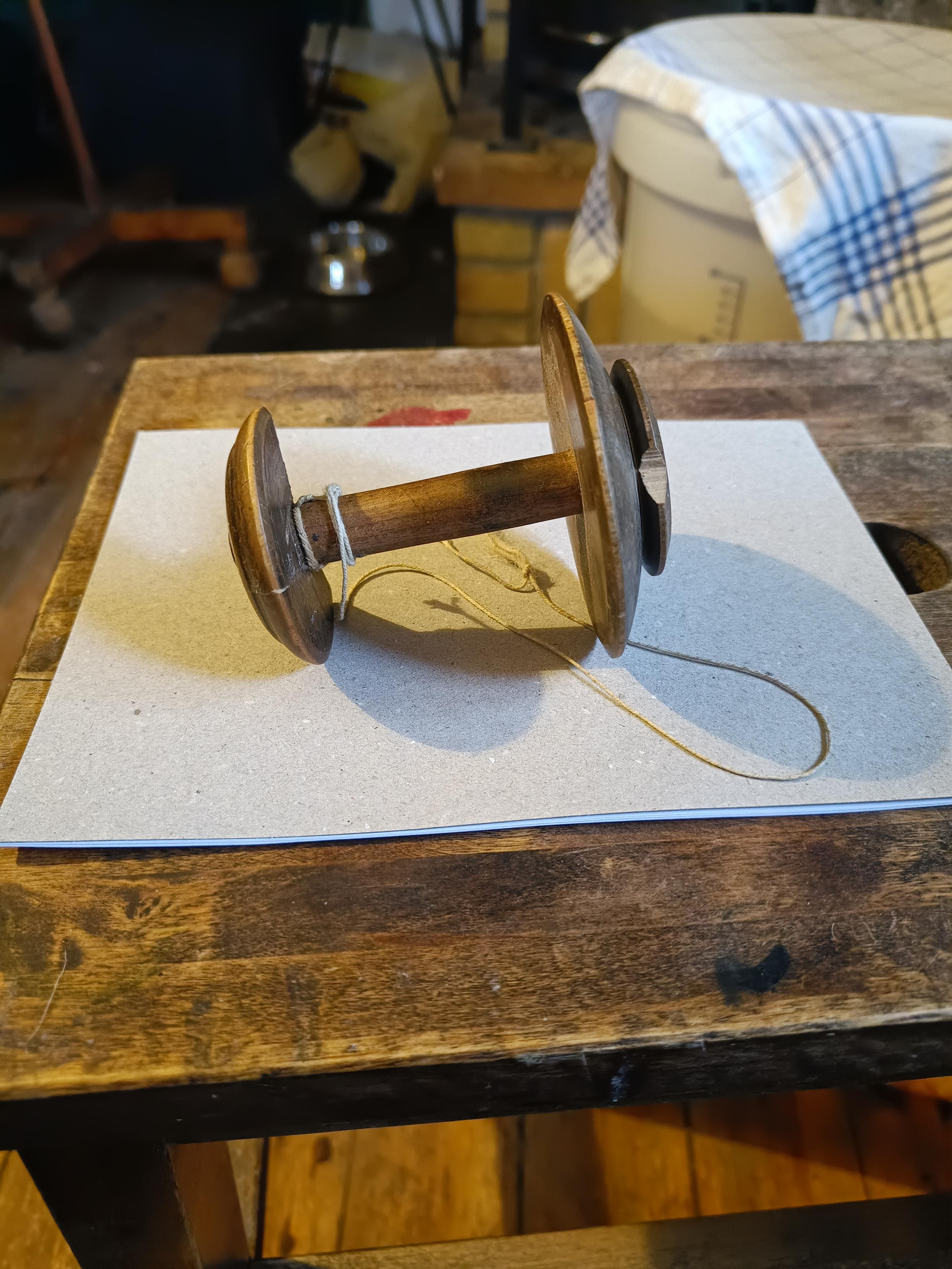 An old wooden spool seen side on. The end caps are different diameters - the larger one, on the right, has a flange with a chip missing.