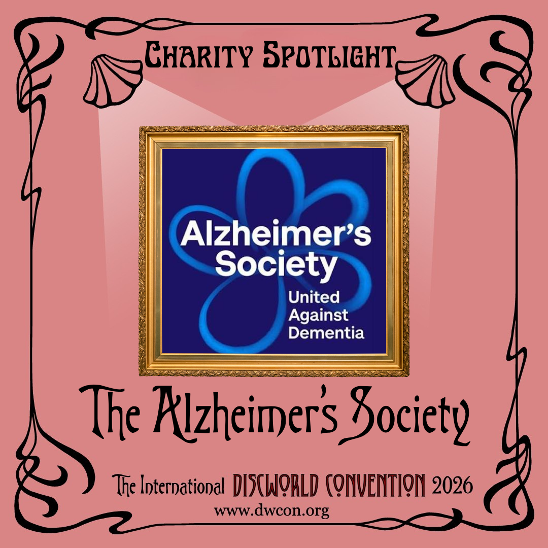 Black text on a pale red background with a black Art Nouveau border. The text reads "Charity Spotlight: The Alzheimer's Society".

At the centre is a golden picture frame 'lit' by two cartoon spotlights. In the frame is the Alzheimer's Society of a logo of a pale blue forget-me-not flower on a navy background. Their slogan reads "United Against Dementia"