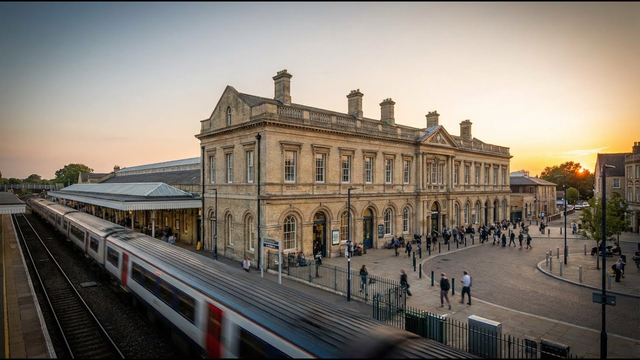 a station with a smart neoclassical building at right angles to the tracks with a pick-up / drop-off roundabout in the corner between the tracks and the building