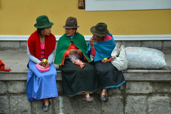 3 Ecuadoraanse vrouwen zitten op een randje met fruit in hun handen te kletsen met elkaar