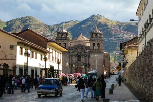 straat met wandelende mensen en blauwe auto en kathedraal in cusco peru