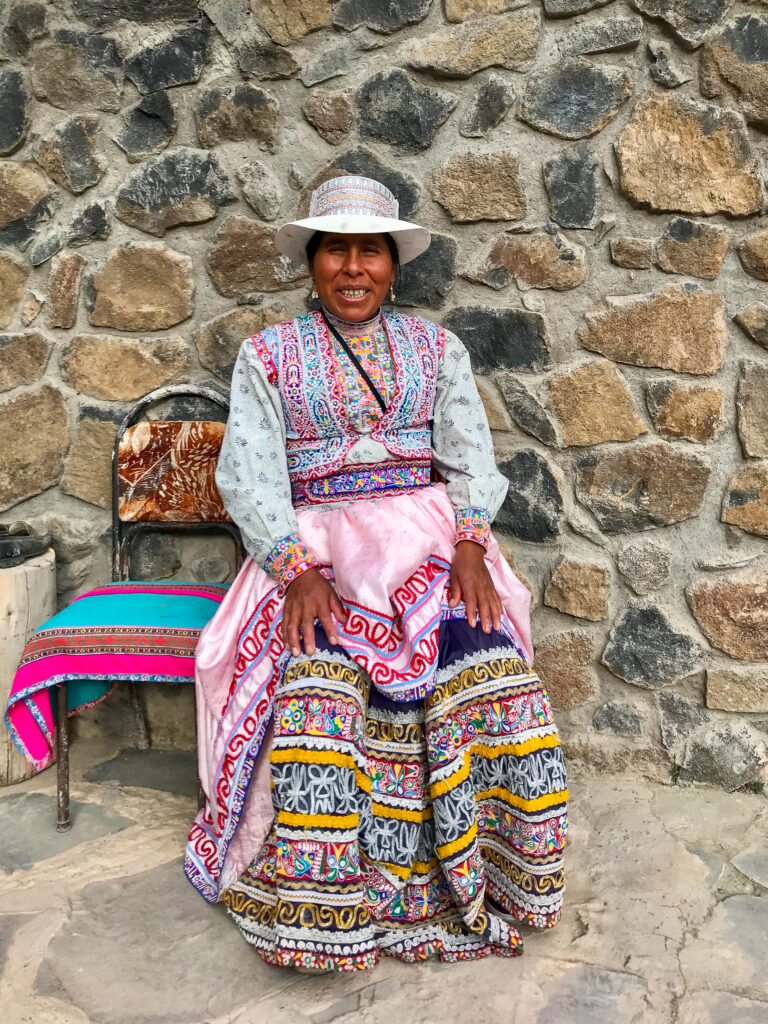 peruaanse vrouw in traditionele kleding die zit op een stoel voor een stenen muur
