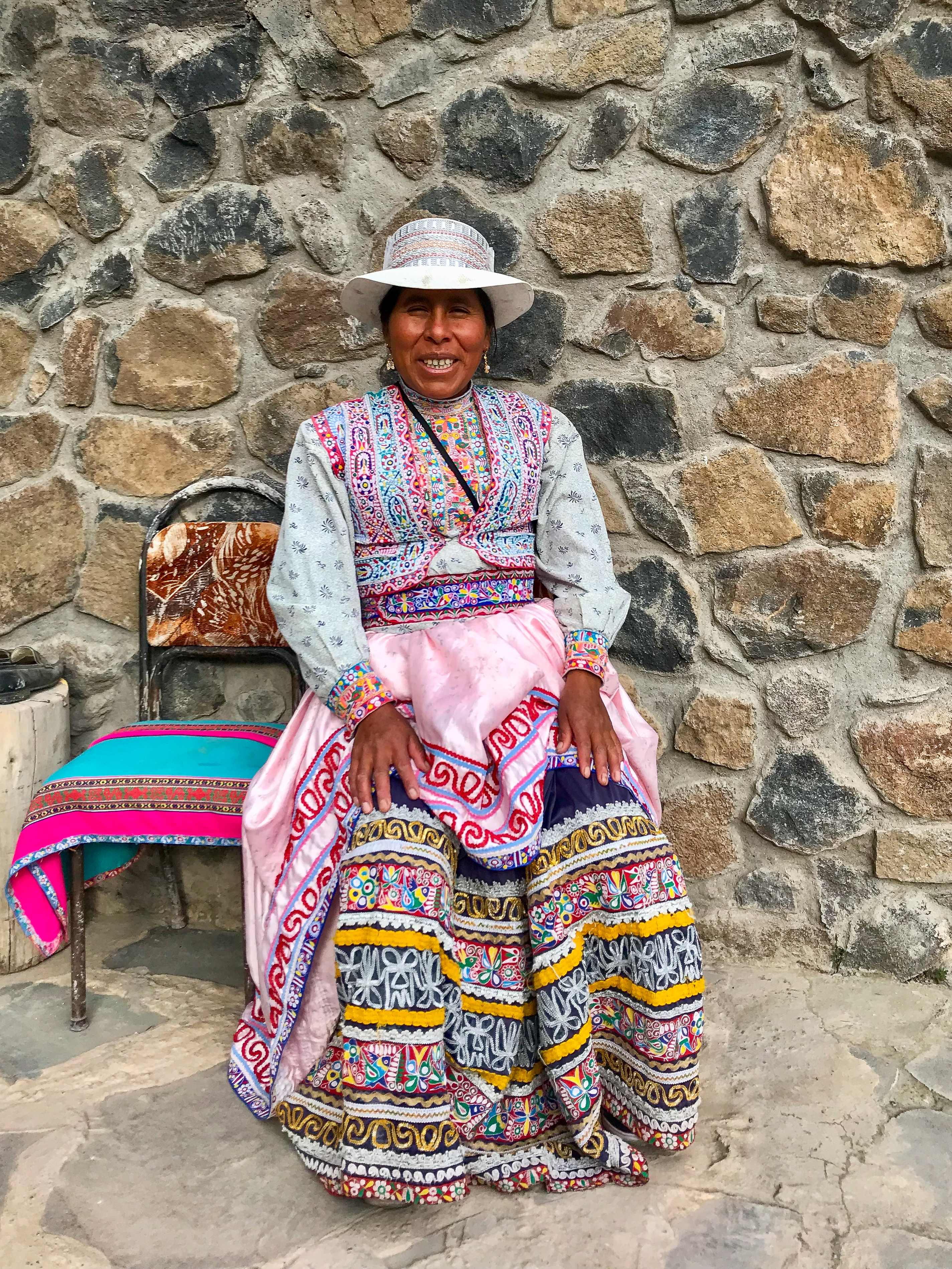 peruaanse vrouw in traditionele kleding die zit op een stoel voor een stenen muur