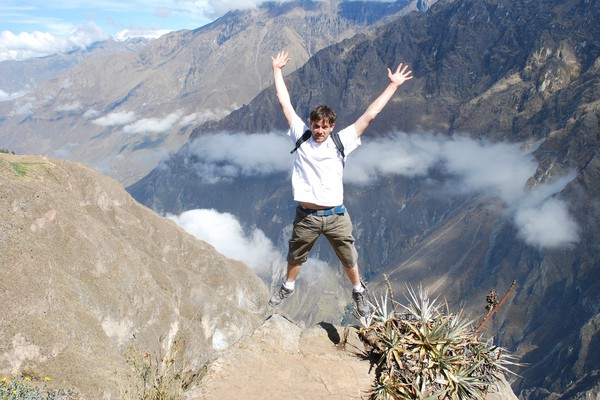 Een man die op de canyon van Peru staat en springt met zijn handen in de lucht