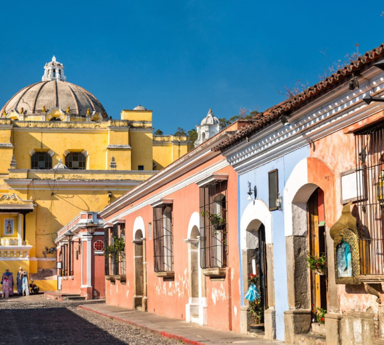 Gekleurde rijtjeswoningen met op de achtergrond een geel gebouw in Antigua Guatemala