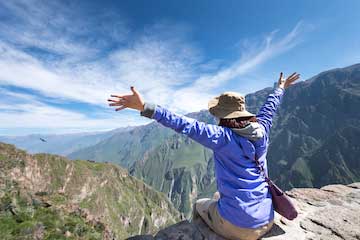 toerist zittend op de rand van een rots kijkend naar het uitzicht over de colca canyon