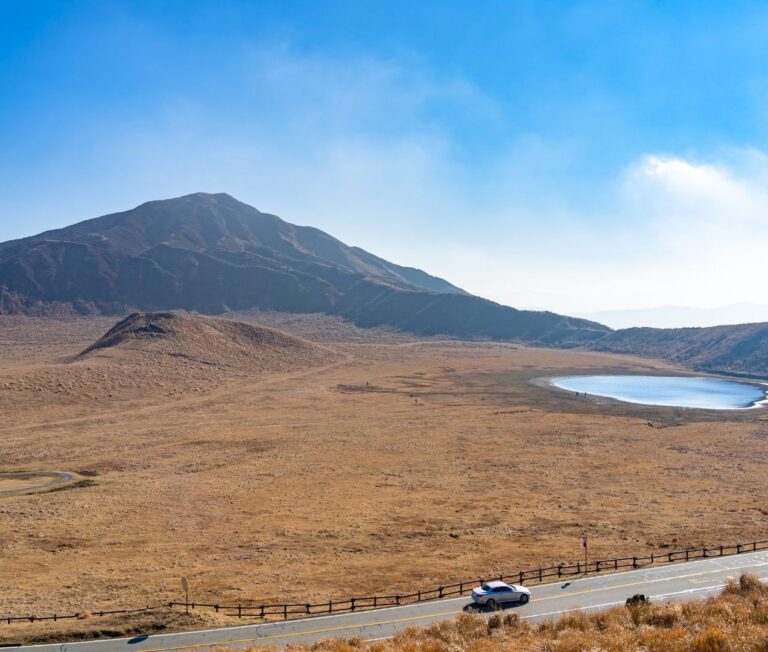 Auto rijdt door het uitgestrekte vulkanische landschap met Kusasenri-grasland bij de Mount Aso vulkaan in Japan