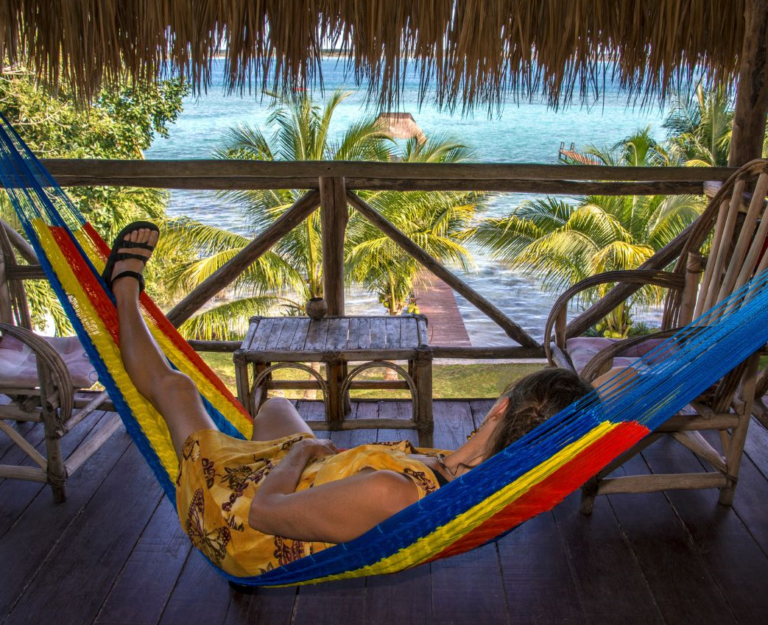 Reiziger liggend in hangmat op het balkon met uitzicht op de palmbomen en de zee