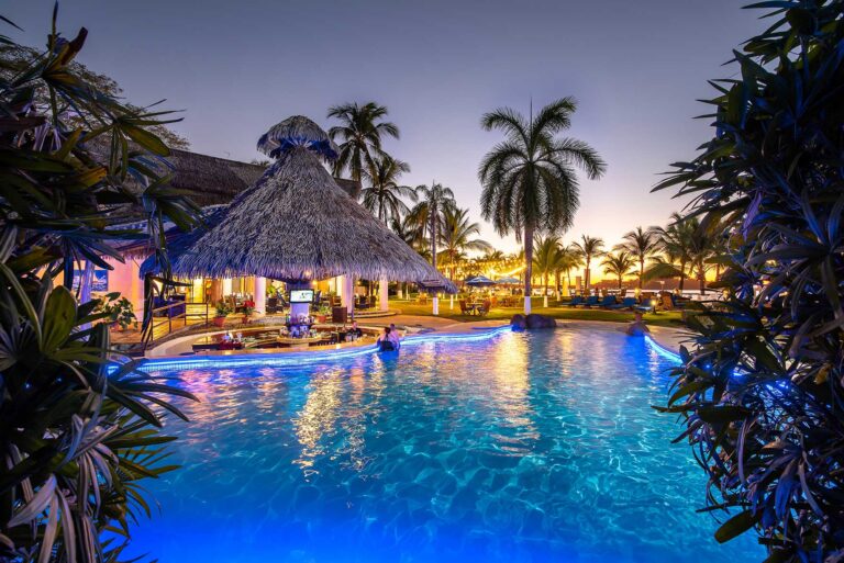 resort zwembad bij avondlicht met rieten bar en palmen