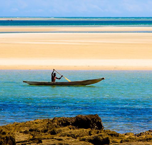 Man in bootje op water en op de achtergrond strand in Madagaskar