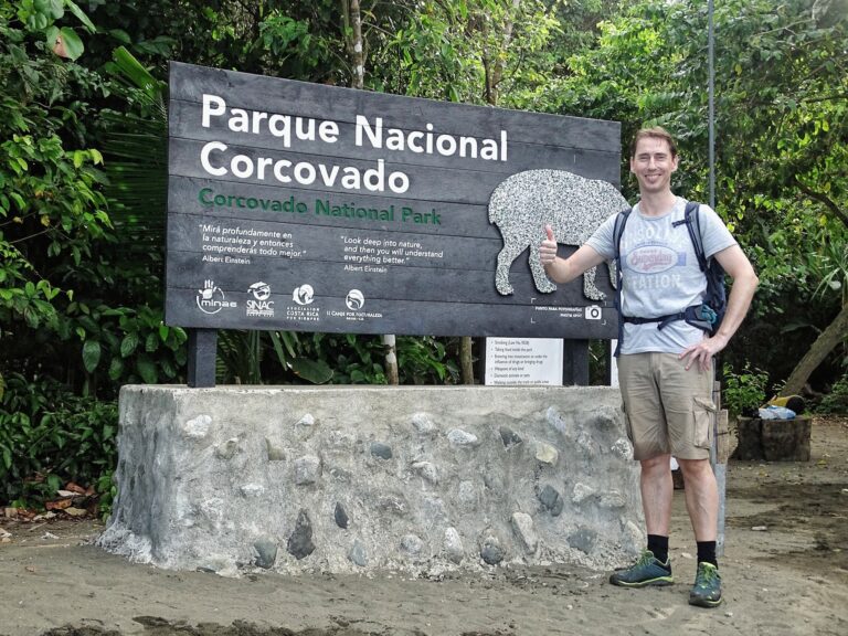 man staat met duim omhoog voor ingangsbord Parque Nacional Corcovado