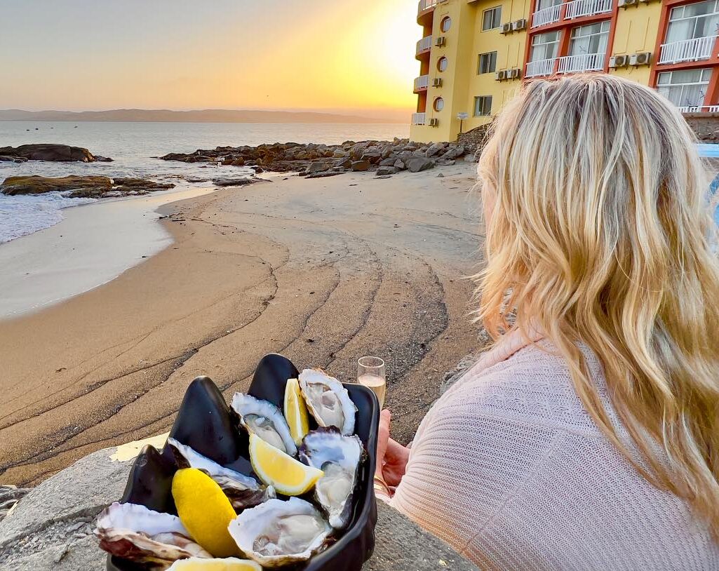 vrouw eet oesters met wijn aan zee bij zonsondergang in swakopmund