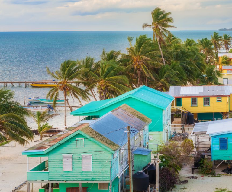 Blauwe huisjes op het strand van Caye Caulker en omringd door palmbomen met op de achtergrond de zee
