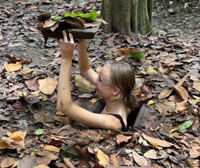 een vrouw komt slechts met haar hoofd en schouders uit boven een krappe Vietnamese tunnel uit de Vietnam-oorlogstijd, zij houd het houtje dat als deksel kan fungeren boven haar hoofd.