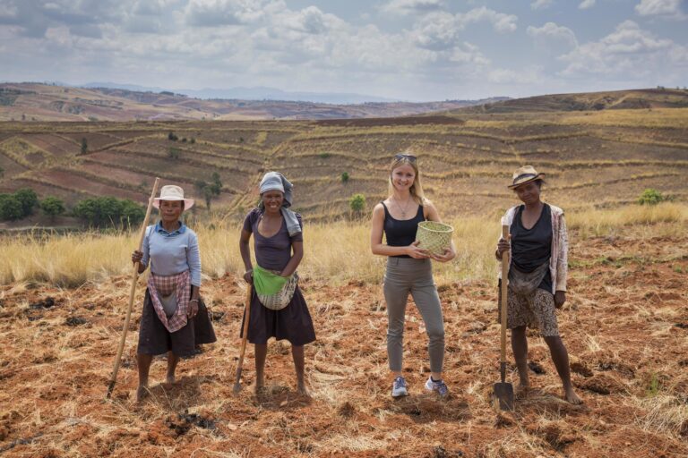 Reiziger staat tussen de locals lachend naar de camera tussen de landbouw en met heuvels op de achtergrond in Madagaskar
