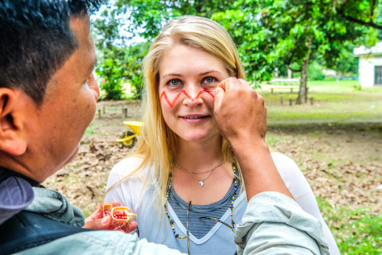 een toerist wordt geschminkt op haar gezicht door een Ecuadoraanse man