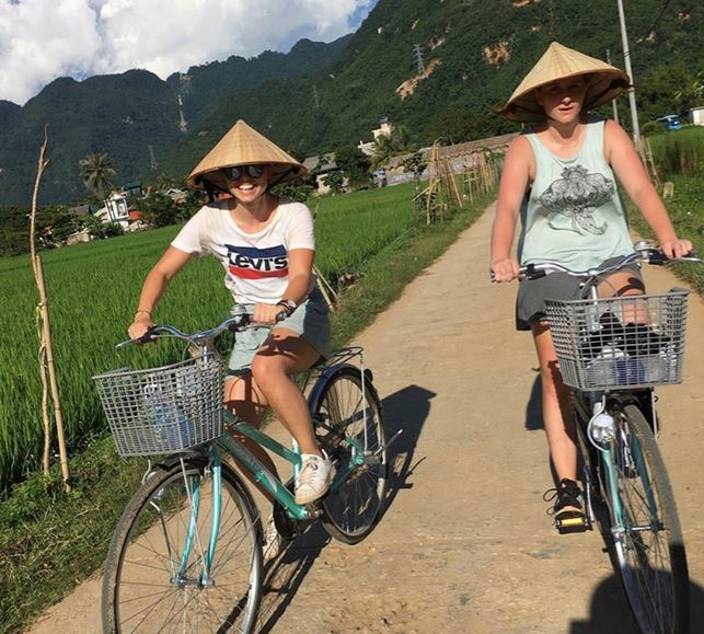 twee mensen fietsen met Vietnamese hoedjes op door de rijstvelden