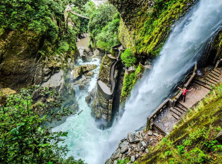 van bovenaf een hele hoge waterval, halverwege op een plateau staat een man met zijn armen wijd