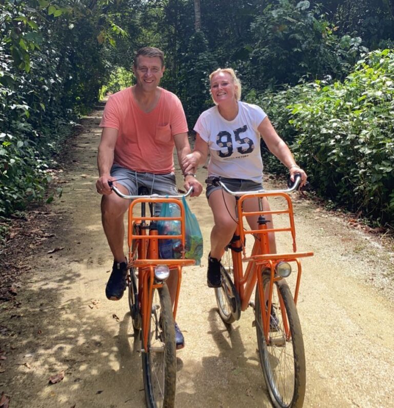 twee mensen fietsen op oranje fiets over zandpad in suriname