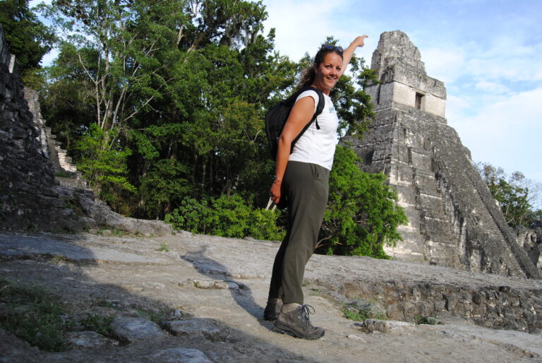 Reiziger lachend naar de camera en met de vinger wijzend naar de top van een Maya ruïne in Tikal Guatemala