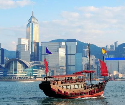 Traditionele Chinese jonk vaart voor de skyline van Hongkong en Victoria Harbour