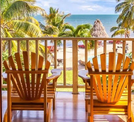 Balkon met twee stoelen uitkijkend op het strand met palmbomen en de zee in Belize
