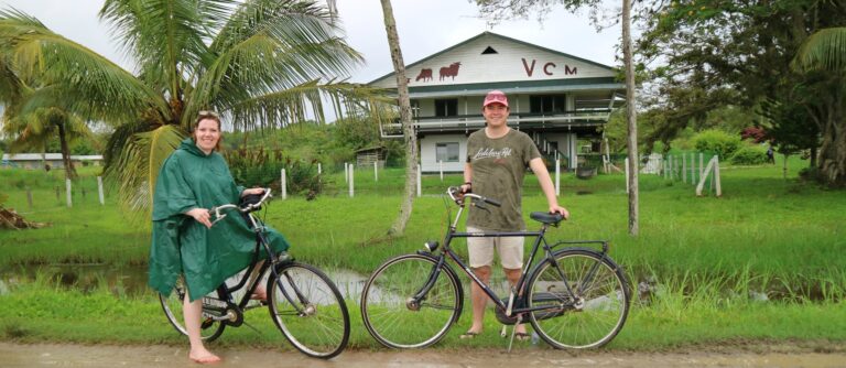 mensen poseren met fiets en in regenkleding op zandpad in Suriname