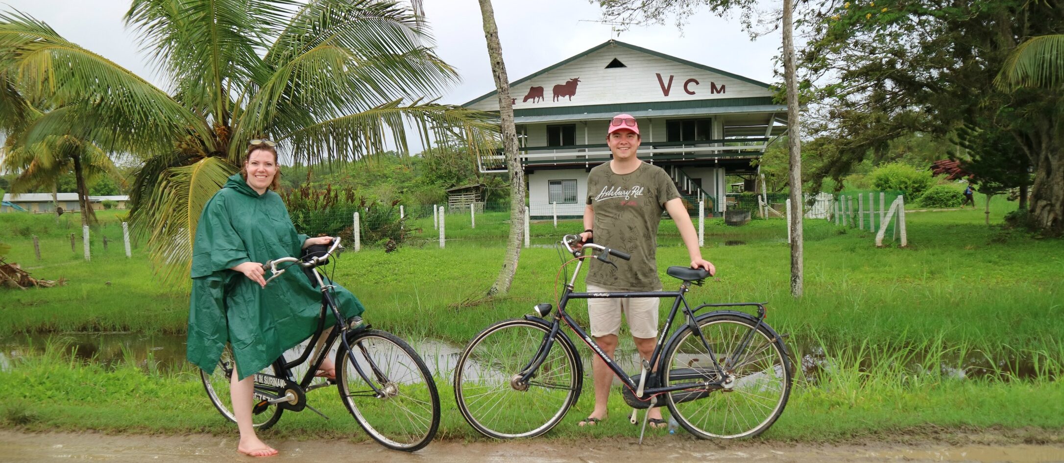 mensen poseren met fiets en in regenkleding op zandpad in Suriname